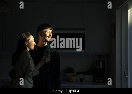 Un jeune couple heureux qui regarde loin en se tenant dans la cuisine Banque D'Images