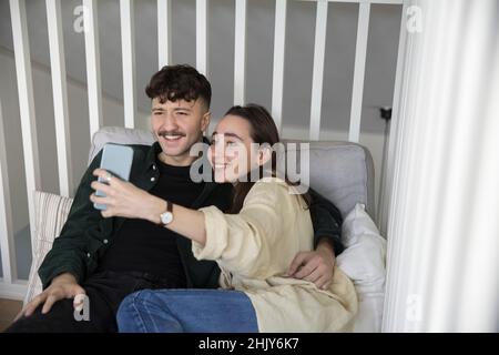 Un jeune couple heureux prend le selfie sur un smartphone dans la chambre Banque D'Images