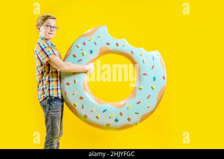 Un garçon mignon tient un énorme donut dans ses mains.Adolescent joyeux.Confiserie.Délicieux dessert.Un gars avec un visage drôle.Vue latérale Banque D'Images