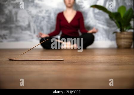 Femme consciente méditant à la maison avec des bâtons d'encens brûlants, se sitant dans la pose de lotus. Tenir les mains sur les genoux avec les paumes orientées vers le haut. Banque D'Images