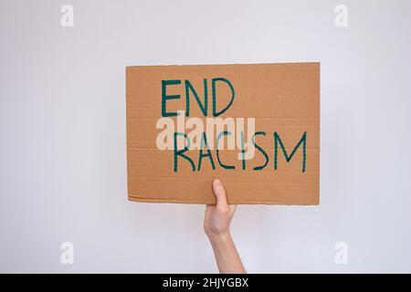 Main tenant le carton avec l'inscription « fin racisme » sur fond de mur gris.La femme proteste contre le racisme. Banque D'Images