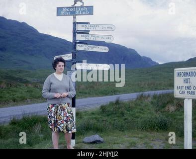 1960s, historique, une dame dans une jupe fleurie et un chandail debout au bord d'un panneau métallique du club de ski écossais, avec diverses flèches directionnelles pour les principales montagnes ou munros de la région, Perth & Kinross, Highlands, Écosse, Royaume-Uni. Sur l'une des flèches 'Scottish ski Club Hut' 2500 pieds. 3/4 HEURES Le Scottish ski Club (SSC) a été fondé en 1907 pour promouvoir le ski en Écosse, comme à l'époque, seulement 50 Écossais possédaient une paire de skis en bois. On voit également une flèche directionnelle pour Ben Lawers, la plus haute montagne de la partie sud des Highlands écossais, Banque D'Images