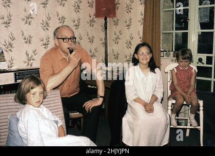 1960s, historique, trois jeunes filles, regardant la télévision avec leur père avant le coucher, Angleterre, Royaume-Uni. Les deux filles plus âgées sont dans leurs robes de nuit et papa fume un tuyau. Banque D'Images