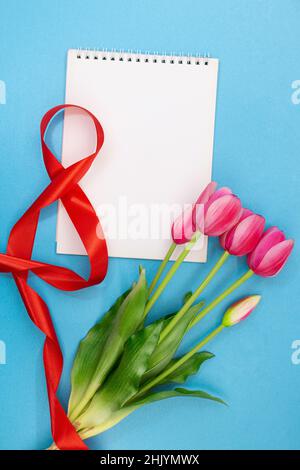 Numéro huit 8 de ruban rouge avec bouquet de tulipes roses et bloc-notes pour le texte sur fond bleu.Holiday, 8 mars, International Women's Banque D'Images