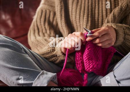 Gros plan d'une femme assise sur un canapé au pull à tricoter à la maison avec laine rose Banque D'Images