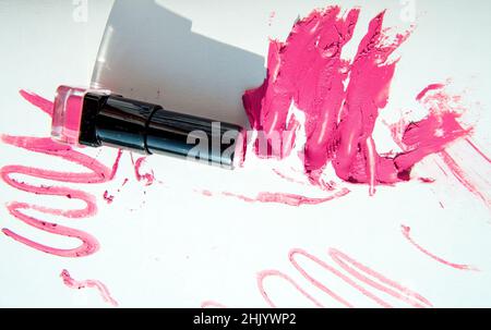 Un tube de rouge à lèvres sur des taches étalées de rouge à lèvres isolées sur un fond blanc.Texture et ombre crémeuses du maquillage.Vue de dessus. Banque D'Images