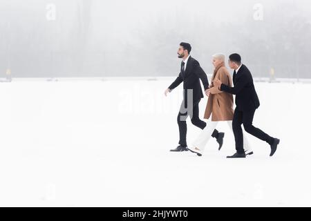 vue latérale d'une femme d'affaires de haut niveau qui traverse un champ enneigé sous la protection de gardes du corps interraciaux Banque D'Images