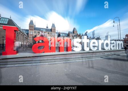 Énorme lettre signe 'I Amsterdam' en face du Rijksmuseum.Longue exposition avec des nuages en mouvement, ciel bleu et touristes flous Amsterdam Hollande Banque D'Images