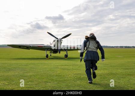 Bataille d'Angleterre bousculant la recréation. Le réacteur pilote de la Royal Air Force de la Seconde Guerre mondiale court vers l'avion de chasse Hawker Hurricane Banque D'Images