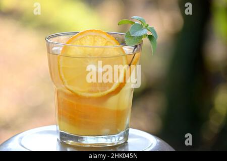 gros plan du bouquet de jus de pamplemousse orange mûr avec de la menthe dans le verre sur fond vert et jaune hors foyer. Banque D'Images