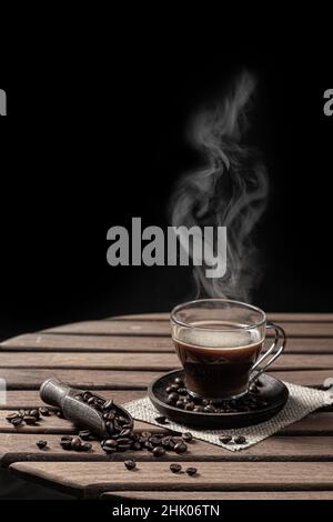 Café chaud dans une tasse en verre et grain de café sur fond noir.Format vertical. Banque D'Images
