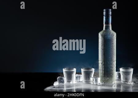 Bouteille de vodka glacée avec verres à liqueur sur fond bleu foncé et espace pour copier. Banque D'Images