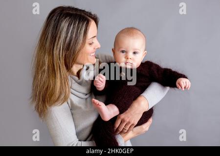 Jeune mère, caressant son nouveau-né garçon, le tenant dans ses bras, différentes positions de tenir bébé, souriant du bonheur Banque D'Images