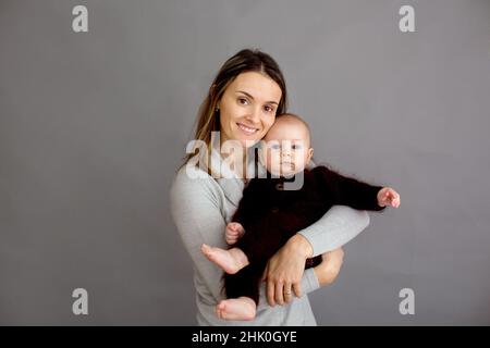 Jeune mère, caressant son nouveau-né garçon, le tenant dans ses bras, différentes positions de tenir bébé, souriant du bonheur Banque D'Images