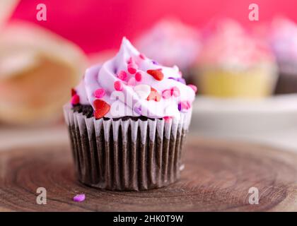 Un cupcake de jour de Saint-Valentin au chocolat sur une dalle en bois et des tulipes et des cupcakes supplémentaires flous dans l'arrière-plan.Fond rose. Banque D'Images