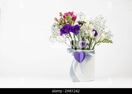 Différentes couleurs beau bouquet de fleurs dans vase blanc vintage avec ruban et coeur de papier sur fond blanc.Vacances romantiques avec cop Banque D'Images