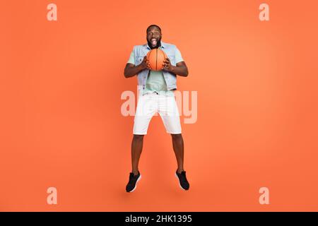Photo de choqué Guy habillé jeans gilet saut haut jouant basket-ball isolé couleur orange fond Banque D'Images