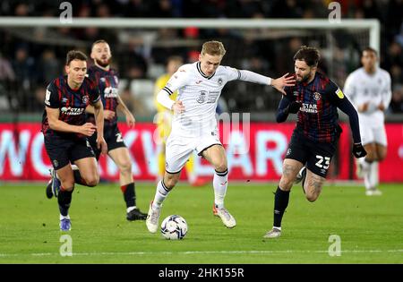 Flynn Downes (au centre) de Swansea City et Henri Lansbury (à droite) de Luton Town se battent pour le ballon lors du match du championnat Sky Bet au stade Swansea.com de Swansea.Date de la photo: Mardi 1 février 2022. Banque D'Images