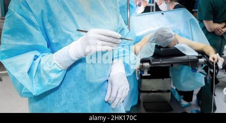 Chirurgien au scalpel dans la salle d'opération.Mise au point sélective.Un médecin portant un uniforme d'opération bleu et des gants stériles tient un scalpel. Banque D'Images