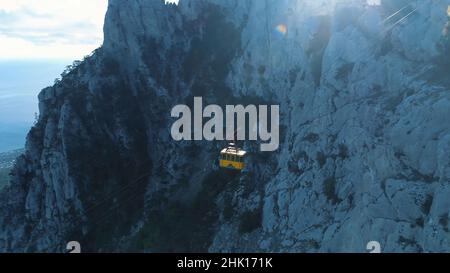 Vue aérienne de l'ascenseur jaune se déplaçant sur le téléphérique près de la pente de haute montagne couverte d'arbres et d'arbustes.Magnifique station d'été Banque D'Images