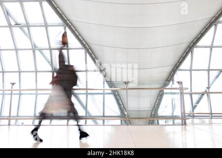 Une personne non identifiable marchant en mouvement flou sur un couloir blanc avec de grandes fenêtres. Des personnes floues marchant dans un bâtiment moderne. Banque D'Images