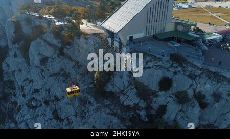 Vue aérienne de l'ascenseur jaune se déplaçant sur le téléphérique près de la pente de haute montagne couverte d'arbres et d'arbustes.Magnifique station d'été Banque D'Images