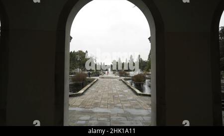 Vue de l'arche sur les personnes marchant dans un beau parc avec des fontaines et un étang contre le ciel gris nuageux.Entrée au parc Banque D'Images