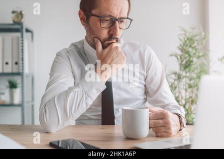 Portrait d'un homme d'affaires perturbé avec une tasse de café au bureau regardant l'écran d'ordinateur portable et la pensée, sélectif foyer Banque D'Images