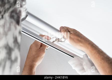 Un homme installe un rideau dans un appartement.Amélioration et décoration de l'intérieur de la maison. Banque D'Images