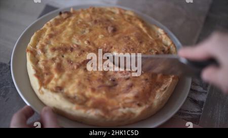 Gros plan des mains coupant une tarte fraîchement cuite sur une plaque de verre dans la cuisine.Couper un morceau de tarte délicieux avec croustillant à l'aide d'un couteau. Banque D'Images