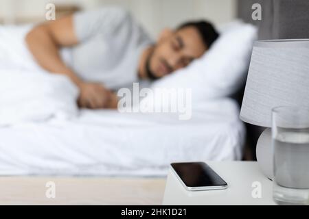 Homme arabe dormant dans un lit avec un smartphone vierge allongé sur une table de chevet Banque D'Images