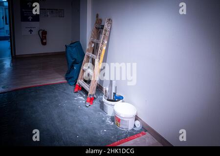 un escabeau en bois et un seau de peinture se trouvent sur le mur dans un couloir Banque D'Images