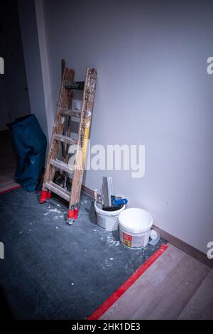 un escabeau en bois et un seau de peinture se trouvent sur le mur dans un couloir Banque D'Images