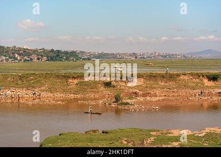 Antananarivo, Madagascar - 07 mai 2019: Personnes travaillant près de la rivière le jour ensoleillé - pêche, faire de la lessive, travailler dans les champs, petites collines avec des maisons i Banque D'Images