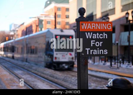 Avertissement attention aux panneaux noir et rouge des trains avec un tramway à l'arrière par temps ensoleillé et neige au sol Banque D'Images