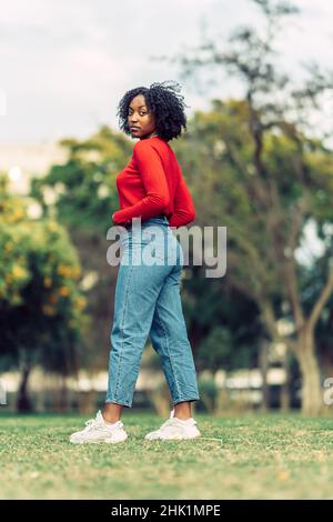 jeune femme aux cheveux noirs bouclés pose avec sa tête tournée en regardant la caméra Banque D'Images