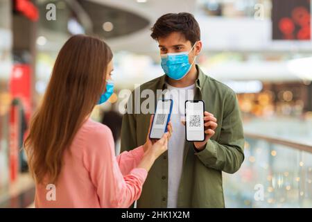Couple portant des masques montrant des téléphones cellulaires avec code QR dans Mall Banque D'Images