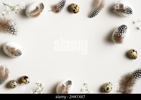 Joyeux Pâques.Cadre fait d'œufs de Pâques élégants décorés de plumes avec des fleurs de gitsophila sur une table blanche.Flat lay, vue de dessus.Minimalistes s Banque D'Images