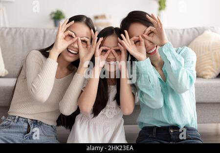 Petite fille asiatique avec sa mère et granny avoir du plaisir, être stupide, faisant des lunettes geste à la maison Banque D'Images