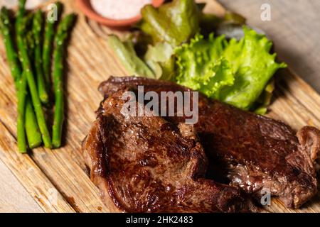 Repas rustique avec deux steaks de bœuf aux asperges vertes et garniture de laitue et une tasse de sel. Banque D'Images