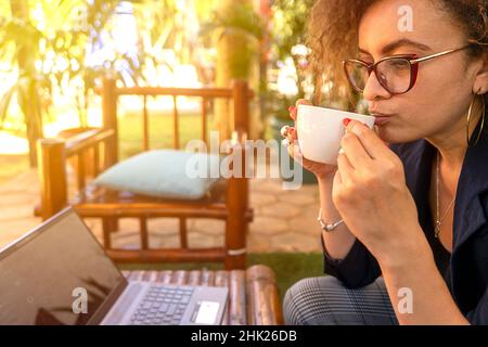 Femme latine aux cheveux échaudement solitaire appréciant une tasse de café dans un restaurant tout en travaillant sur son ordinateur Banque D'Images