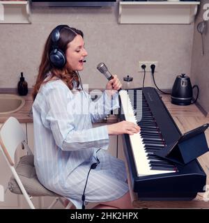 Une musicienne chante dans un microphone et joue du piano dans une cuisine maison Banque D'Images