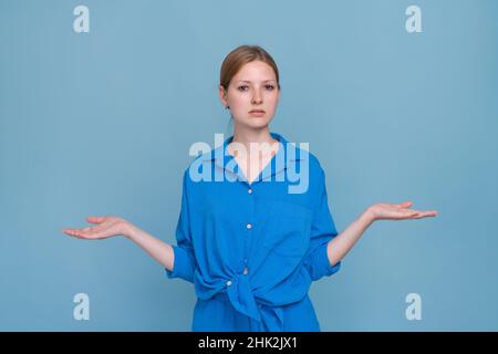 Jeune femme en chemise sur fond bleu, pointant vers le côté avec les deux mains montrant quelque chose d'étrange et de dire, je ne sais pas ce que c'est.Concept publicitaire.Fille caucasienne posant sur de la couleur en studio Banque D'Images