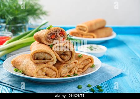 Crêpes farcies à la viande et aux carottes à la crème sure sur fond bleu.Crêpes russes traditionnelles.Vue latérale, espace de copie. Banque D'Images