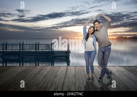 Les couples asiatiques font la forme d'un coeur avec les mains avec un fond de ciel spectaculaire.Saint-Valentin Banque D'Images