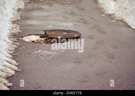 Ouvrir un trou d'homme d'égout brisé sur la route asphaltée d'hiver Banque D'Images