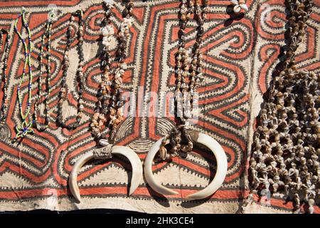 Papouasie-Nouvelle-Guinée, Tufi. Colliers de coquillages avec défenses de sanglier sur tissu traditionnel de tapa fait à la main, en papier mûrier, peint à la main avec natur Banque D'Images