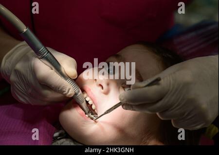 Le dentiste pédiatrique traite les dents de l'enfant, la lumière locale sur le visage du patient, l'examen de la dent après le nettoyage des caries. Banque D'Images