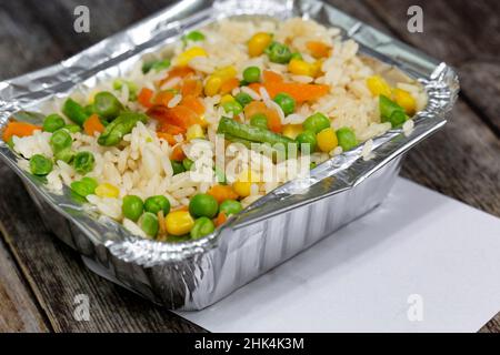 Portion de riz avec légumes mélangés dans un récipient à emporter en papier d'aluminium et couvercle.Sur fond en bois Banque D'Images