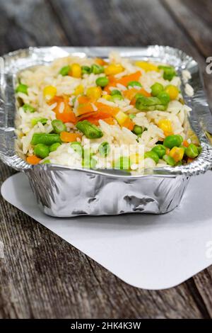 Portion de riz avec légumes mélangés dans un récipient à emporter en papier d'aluminium et couvercle.Sur fond en bois Banque D'Images